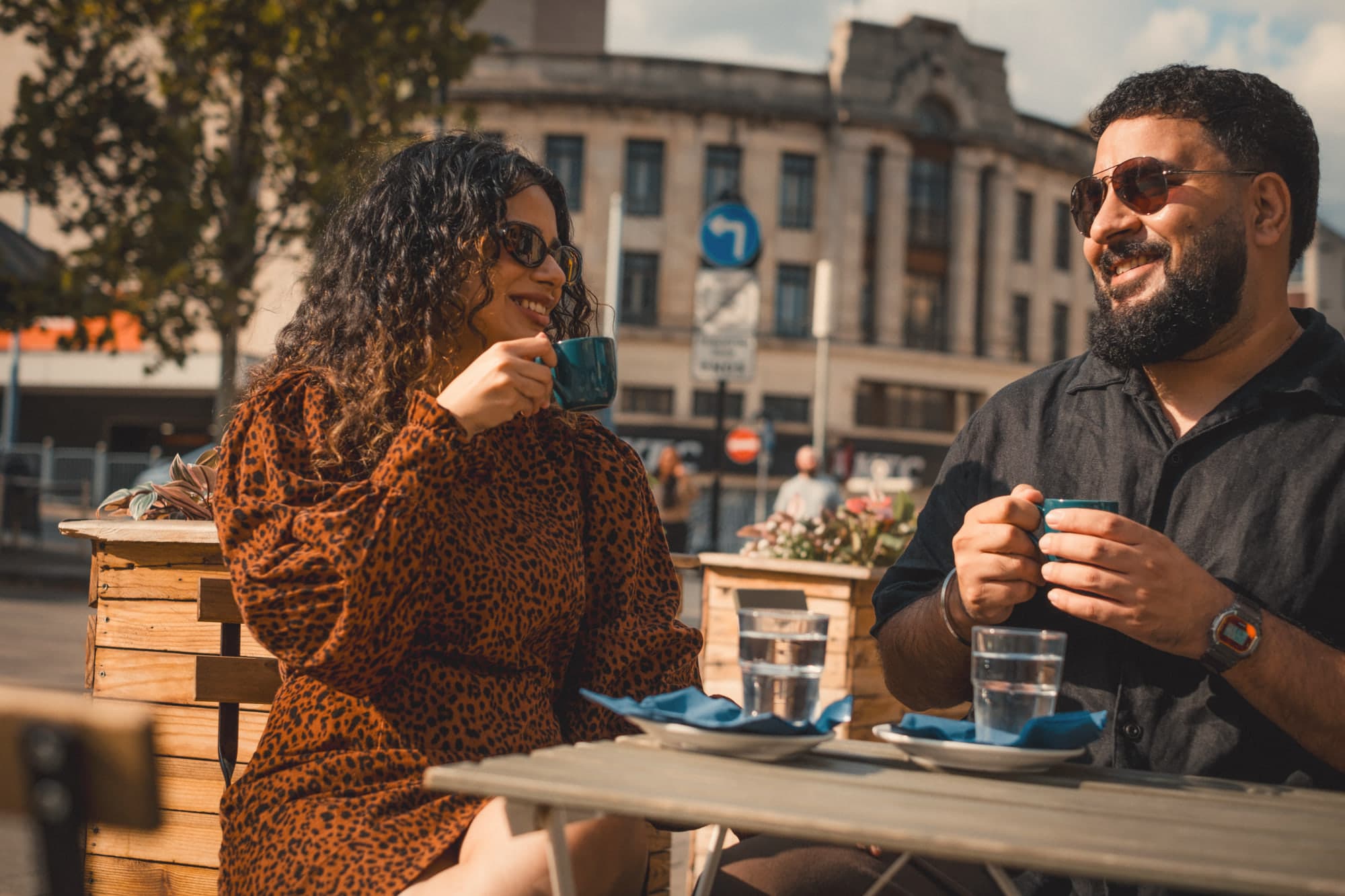 The two of them laughing over coffee at a table in the sun
